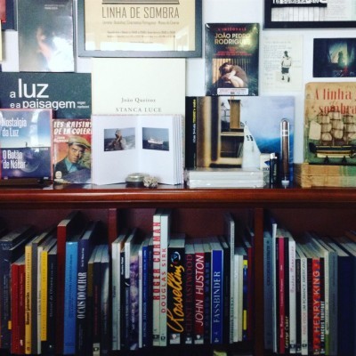 Estante com livros variados e posters culturais na parede