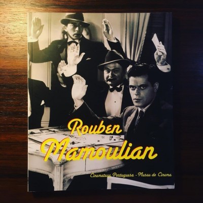 Capa de livro com foto a preto e branco de três homens em traje formal com mãos levantadas