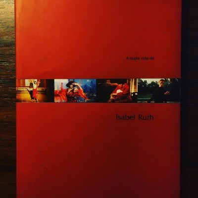 Livro vermelho com título 'A dupla vida de Isabel Ruth' e quatro fotografias coloridas no meio