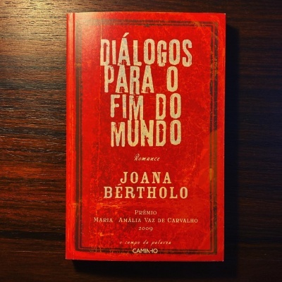 Livro vermelho com texto branco e dourado sobre superfície de madeira