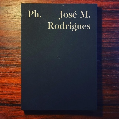 Livro preto com texto branco 'Ph. José M. Rodrigues' sobre mesa de madeira