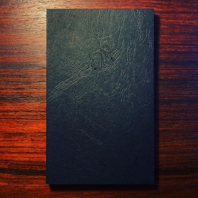 Livro de capa dura preta texturizada sobre mesa de madeira escura