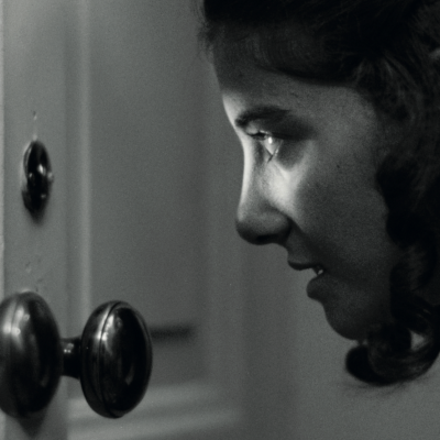 Rapariga a olhar por cima de uma maçaneta antiga numa porta de madeira