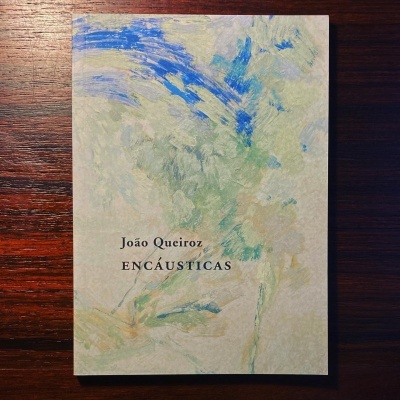 Livro João Queiroz ENCAÚSTICAS com capa abstrata em tons de azul, verde e bege sobre madeira escura