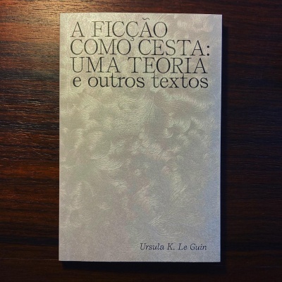 Livro 'A FICÇÃO COMO CESTA: UMA TEORIA e outros textos' de Ursula K. Le Guin sobre mesa de madeira