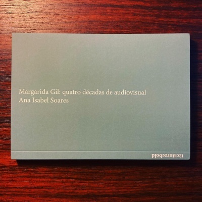 Livro cinzento com texto branco de autor e título sobre mesa de madeira escura