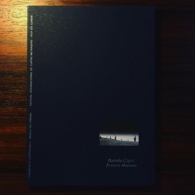 Capa preta de livro com nome dos autores e pequenas imagens centrais sobre mesa de madeira