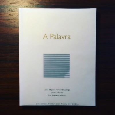 Livro branco intitulado 'A Palavra' com texto e padrão cinzento na capa, sobre mesa de madeira.
