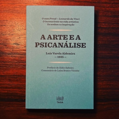 Livro 'A ARTE E A PSICANÁLISE' capa azul claro sobre mesa de madeira