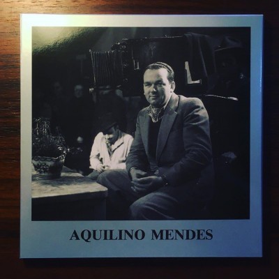 Fotografia a preto e branco de um homem em fato sentado com legenda Aquilino Mendes