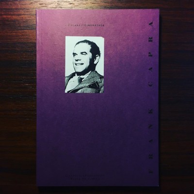 Livro roxo com foto de homem e texto, sobre mesa de madeira escura
