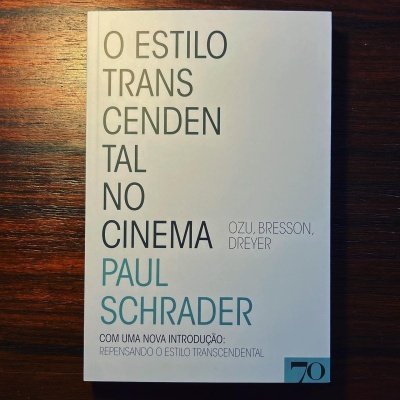 Capa do livro 'O ESTILO TRANSCENDENTAL NO CINEMA' de Paul Schrader sobre mesa de madeira