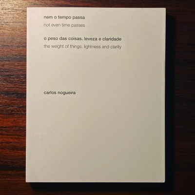 Livro branco com texto em português e inglês colocado sobre superfície de madeira escura