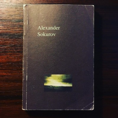 Livro com capa preta e texto Alexander Sokurov sobre superfície de madeira.