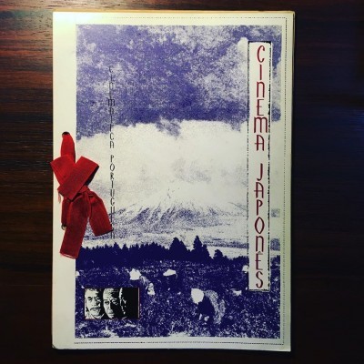 Livro capa branca com ilustração azul, texto 'CINEMA JAPONES' e fita vermelha sobre mesa