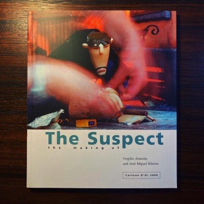 Capa do livro 'The Suspect the making of' com figura animada e mãos desfocadas sobre uma mesa