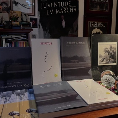 Livros, rolos de filme, fotografia em moldura, taça com líquido e esfera decorativa numa mesa de madeira