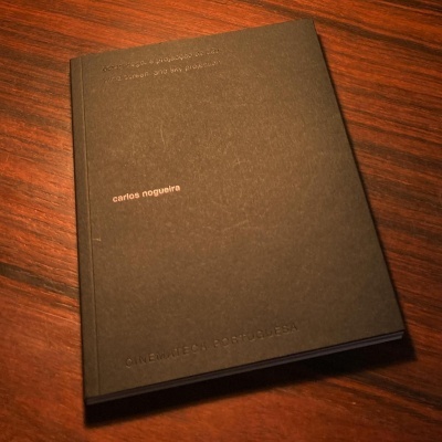 Livro preto de capa dura com texto branco e relevo sobre mesa de madeira