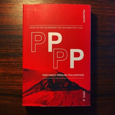 Livro vermelho com texto branco e imagem preta sobre mesa de madeira