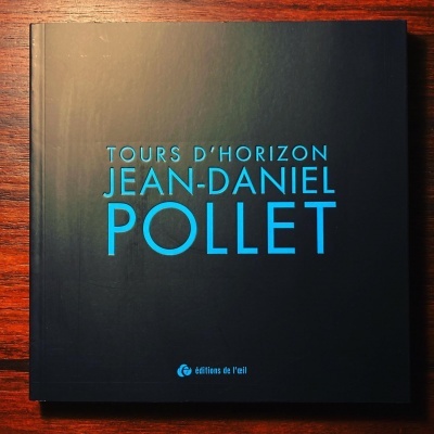 Livro negro com texto azul numa mesa de madeira.