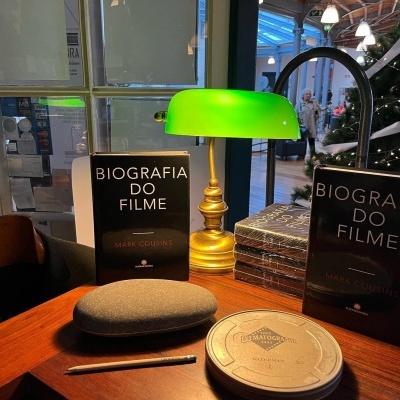 Mesa de madeira com livros, caixas de filme e candeeiro verde e dourado