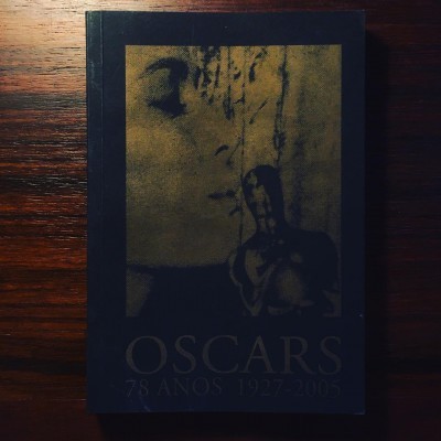 Livro preto e dourado com texto Oscars 78 anos 1927-2005 sobre superfície de madeira