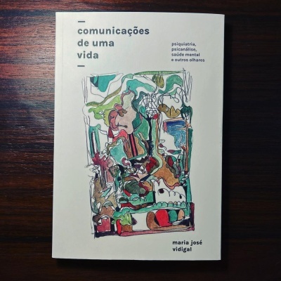 Livro 'comunicações de uma vida' com capa branca e ilustração abstrata colorida sobre fundo de madeira