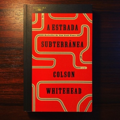 Livro A Estrada Subterrânea de Colson Whitehead com capa vermelha e lombada preta sobre mesa de madeira