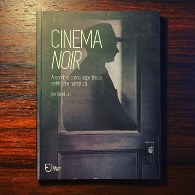 Capa de livro preto com sombra de homem de chapéu atrás de porta escura