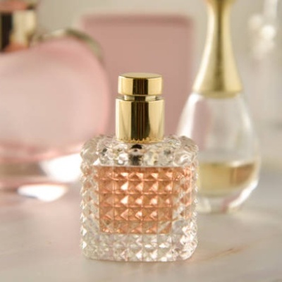 Frasqueira de perfume em vidro com padrão texturizado e tampa dourada, líquido rosa claro