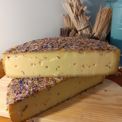 Queijo amarelo com cobertura de flores secas sobre tábua de madeira