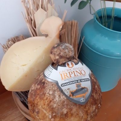 Queijo Caciocavallo Irpino com rótulo branco e laranja numa superfície de madeira junto a vaso azul e ramos secos