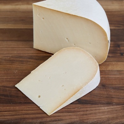 Queijo creme claro com casca branca cortado em duas partes sobre tábua de madeira escura