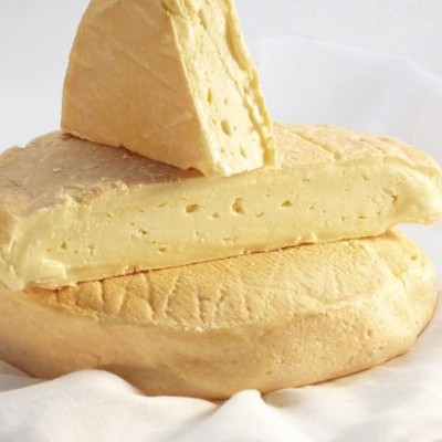 Queijo amarelo pálido com casca rugosa, em duas porções sobre pano branco