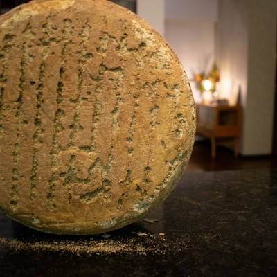 Roda de queijo envelhecido com casca natural texturada sobre superfície escura