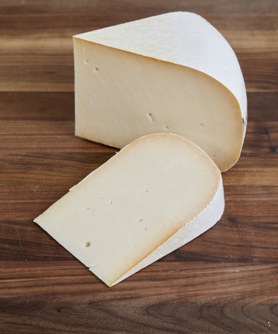 Queijo creme claro com casca branca cortado em duas partes sobre tábua de madeira escura