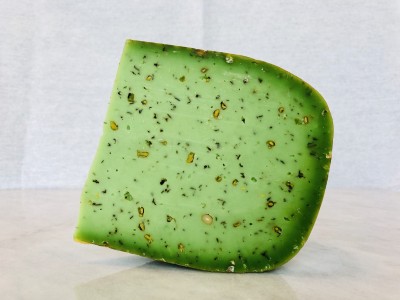 Pedaço de queijo verde com ervas visíveis na massa, sobre superfície clara