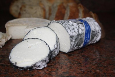 Queijo em rolo cortado sobre granito com pão ao fundo