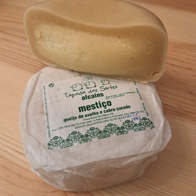 Queijo mestiço curado embalado em papel branco com etiqueta verde e preto sobre madeira clara