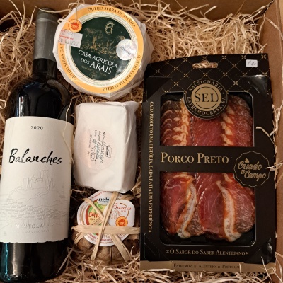 Conjunto de vinho, queijos e enchidos numa caixa com palha