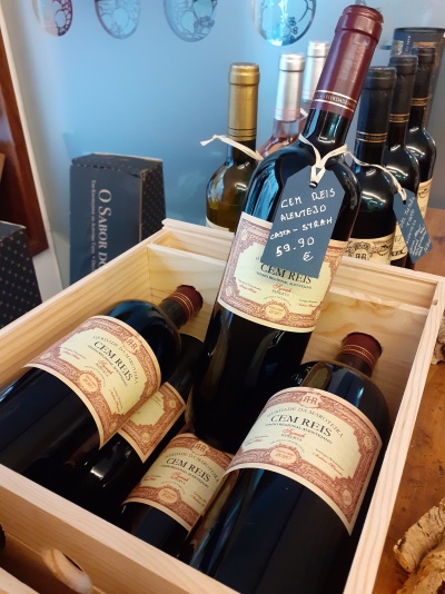 Garrafas de vinho tinto Cem Reis numa caixa de madeira com etiqueta de preço pendurada