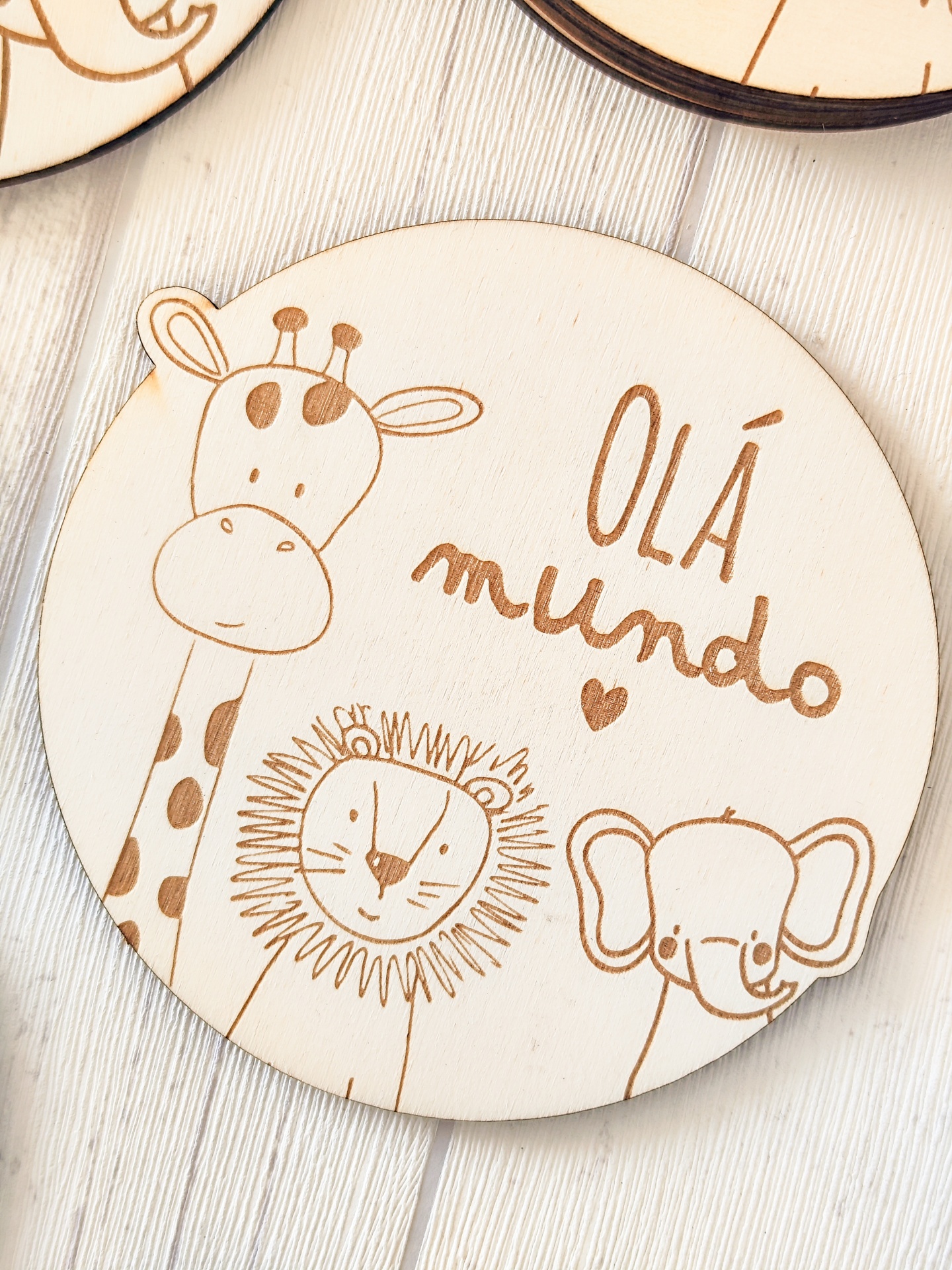 Prato redondo em madeira com desenho de girafa, leão, elefante e texto OLÁ mundo