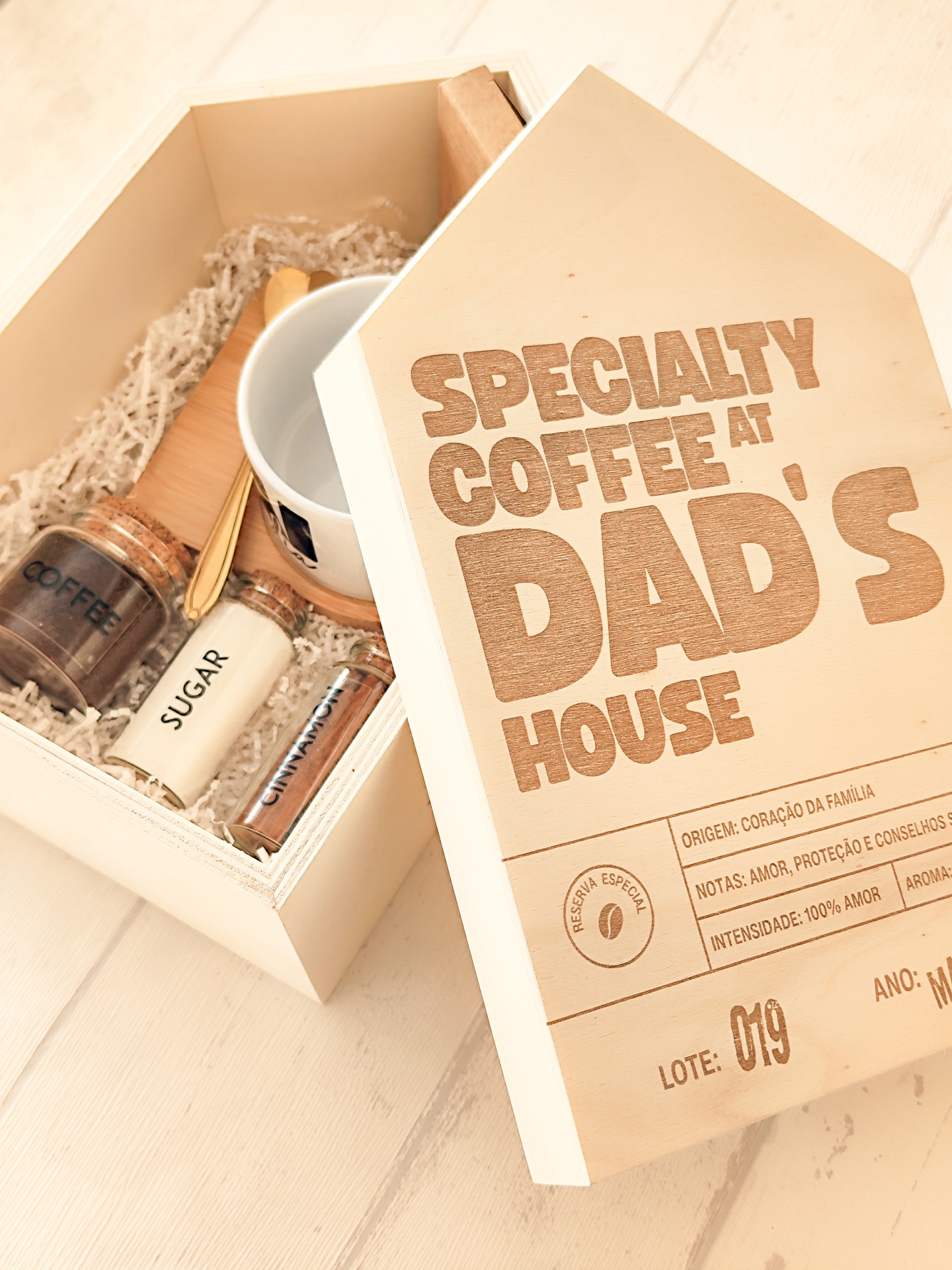 Caixa de madeira clara com tampa gravada e itens para café, incluindo frascos de vidro, chávena e colher