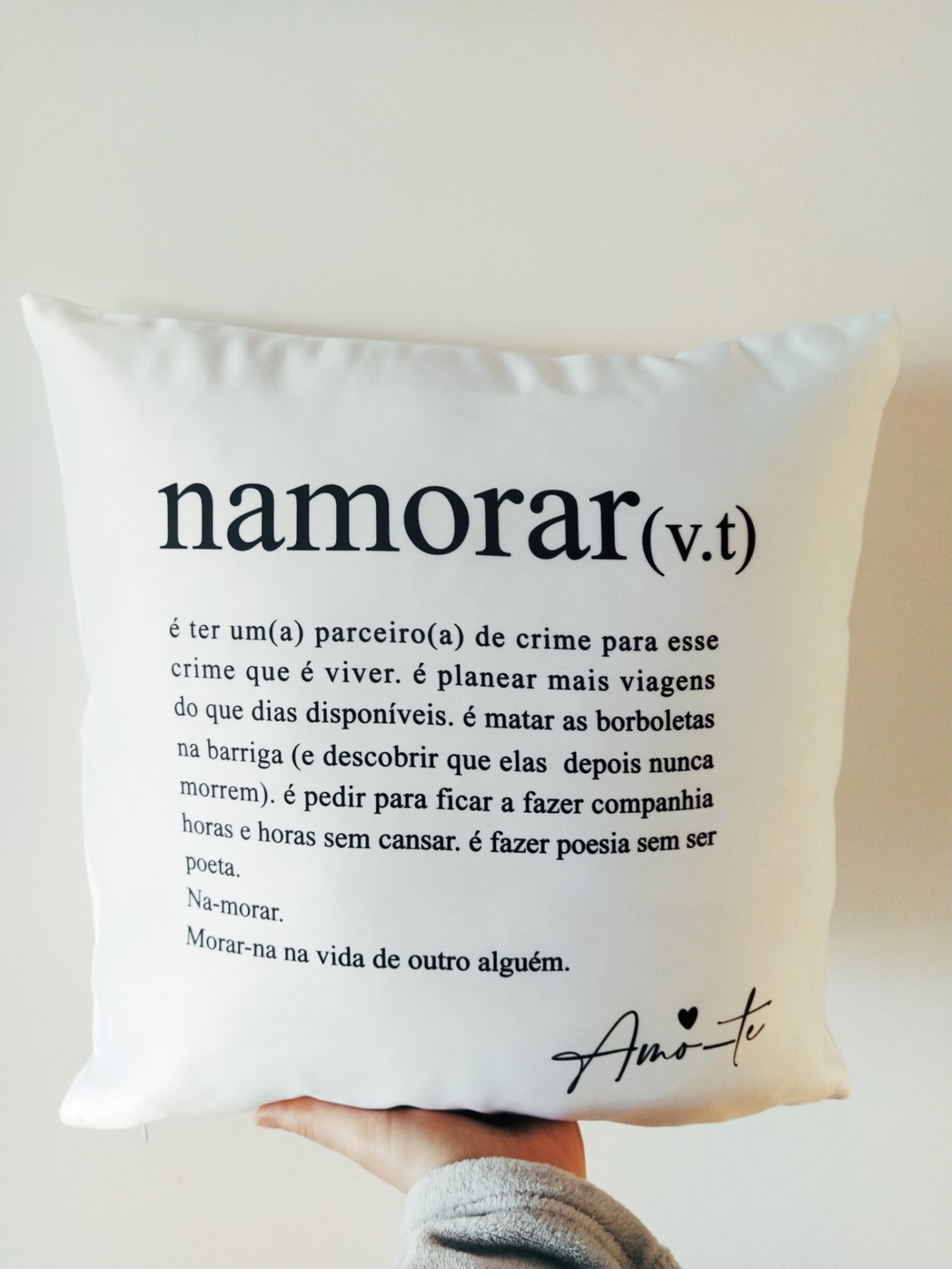 Almofada branca com texto preto e mão segurando