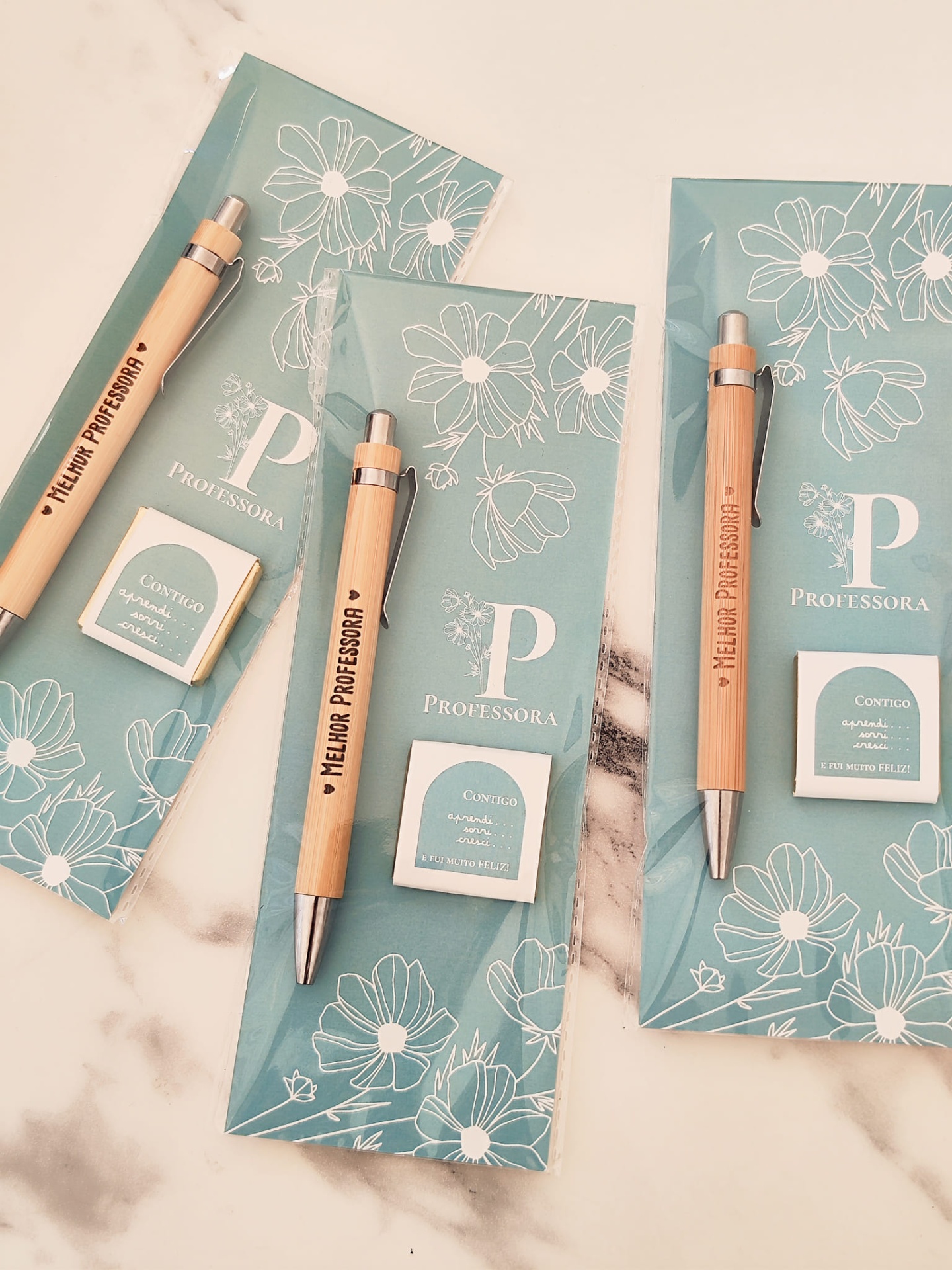 Conjuntos de brindes com canetas de madeira e sabonetes em embalagens azuis com flores brancas