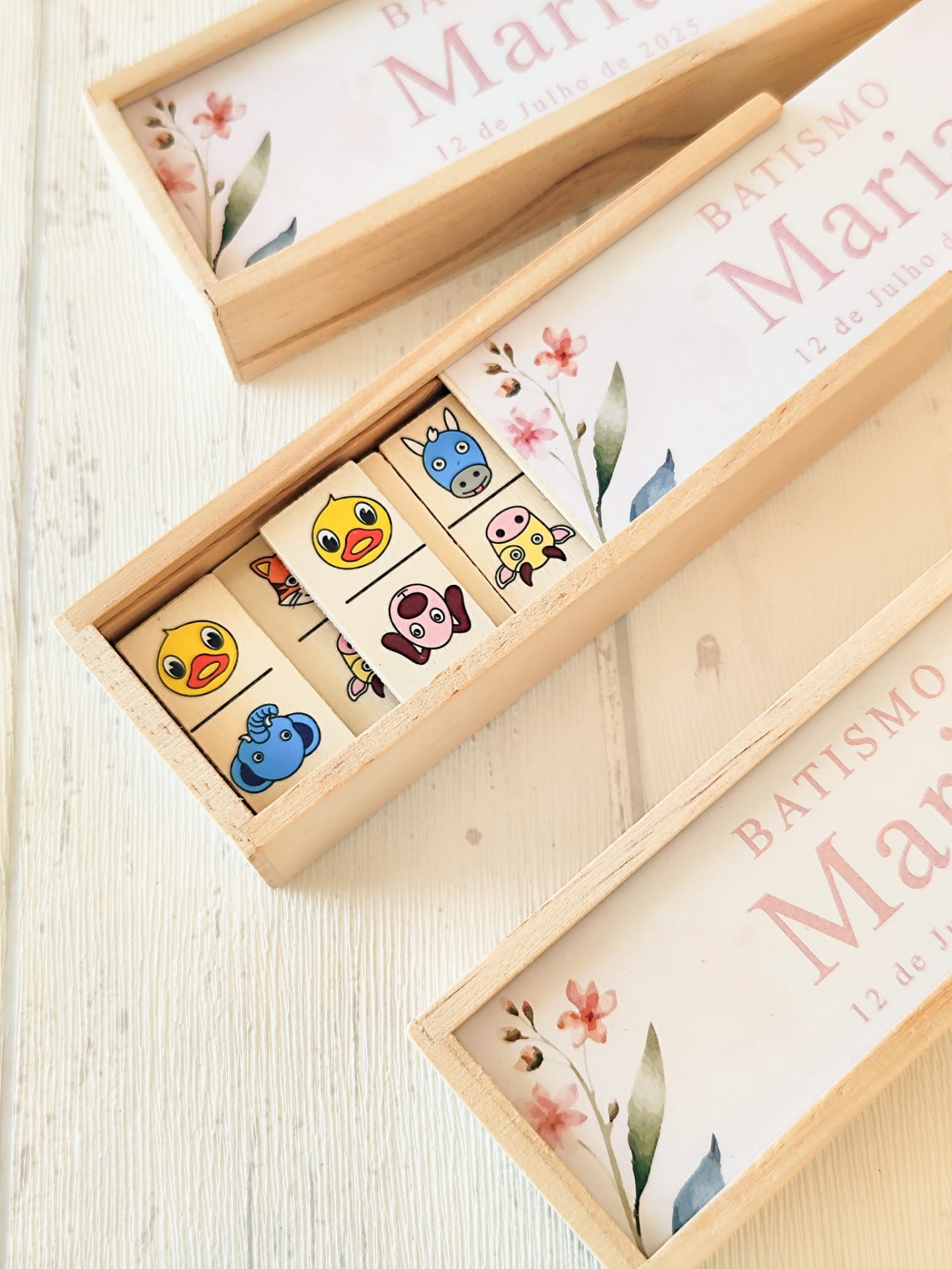 Conjunto de dominós de madeira com desenhos de animais e caixas de madeira claras com texto de batismo