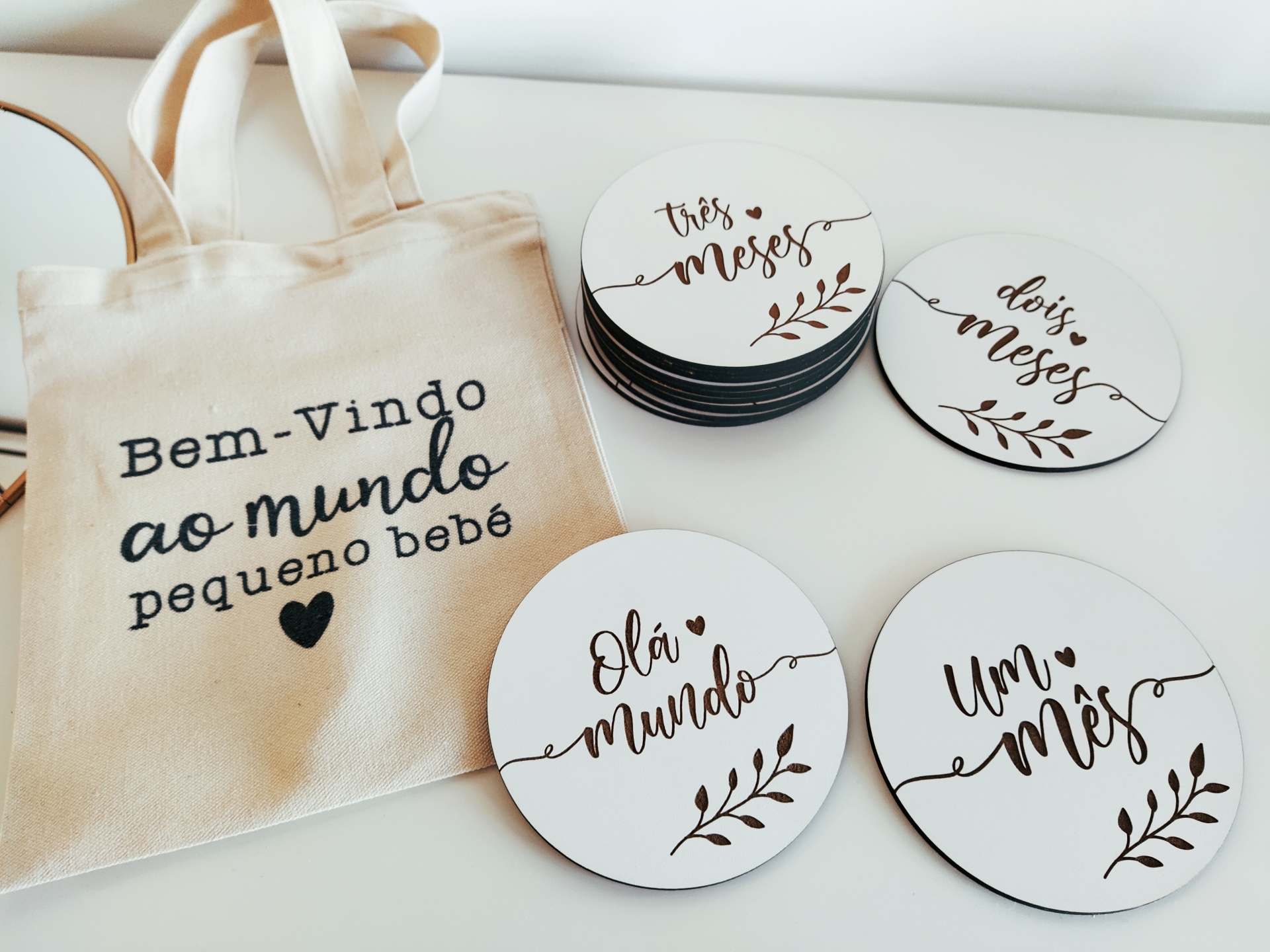 Saco de tecido bege com texto e discos brancos redondos para meses de bebé com letras pretas