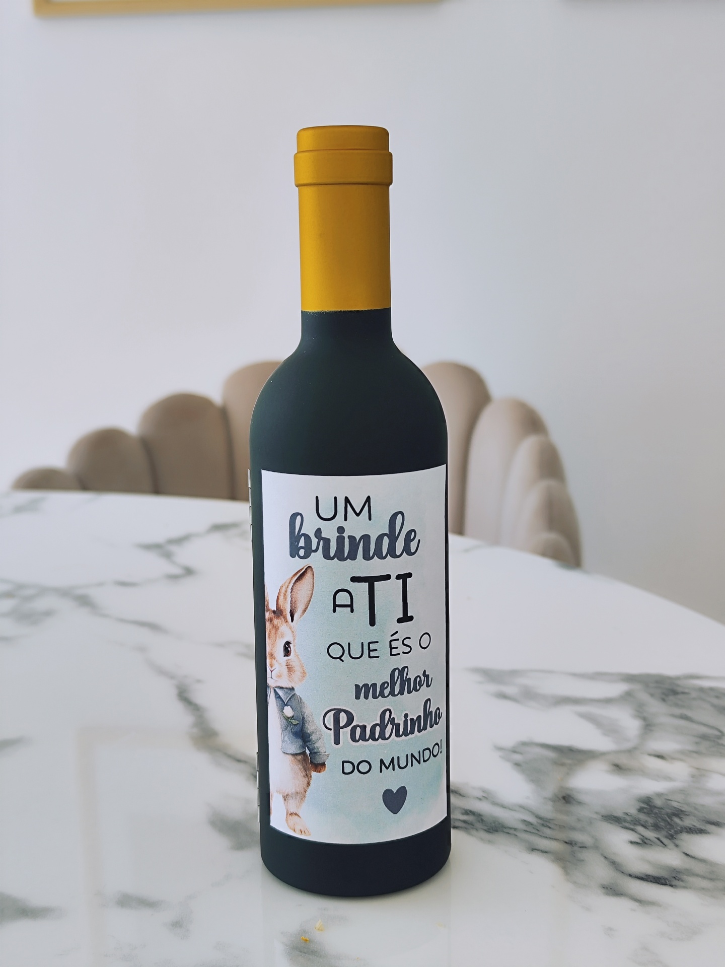 Garrafa decorativa com rótulo e desenho de coelho, tampada em amarelo, sobre mesa de mármore.