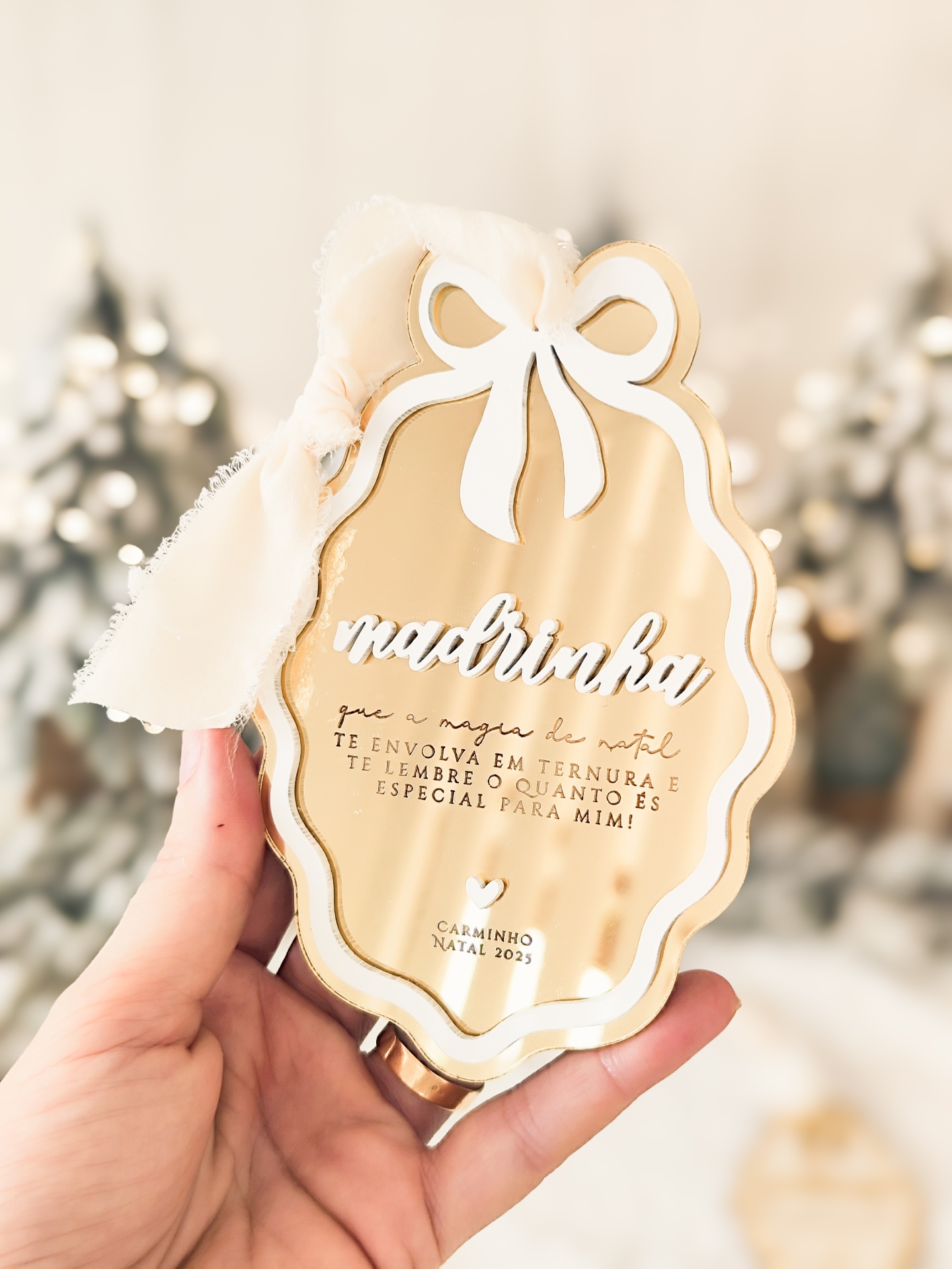 Placa decorativa dourada com laço branco e texto em relevo sobre tema Natal