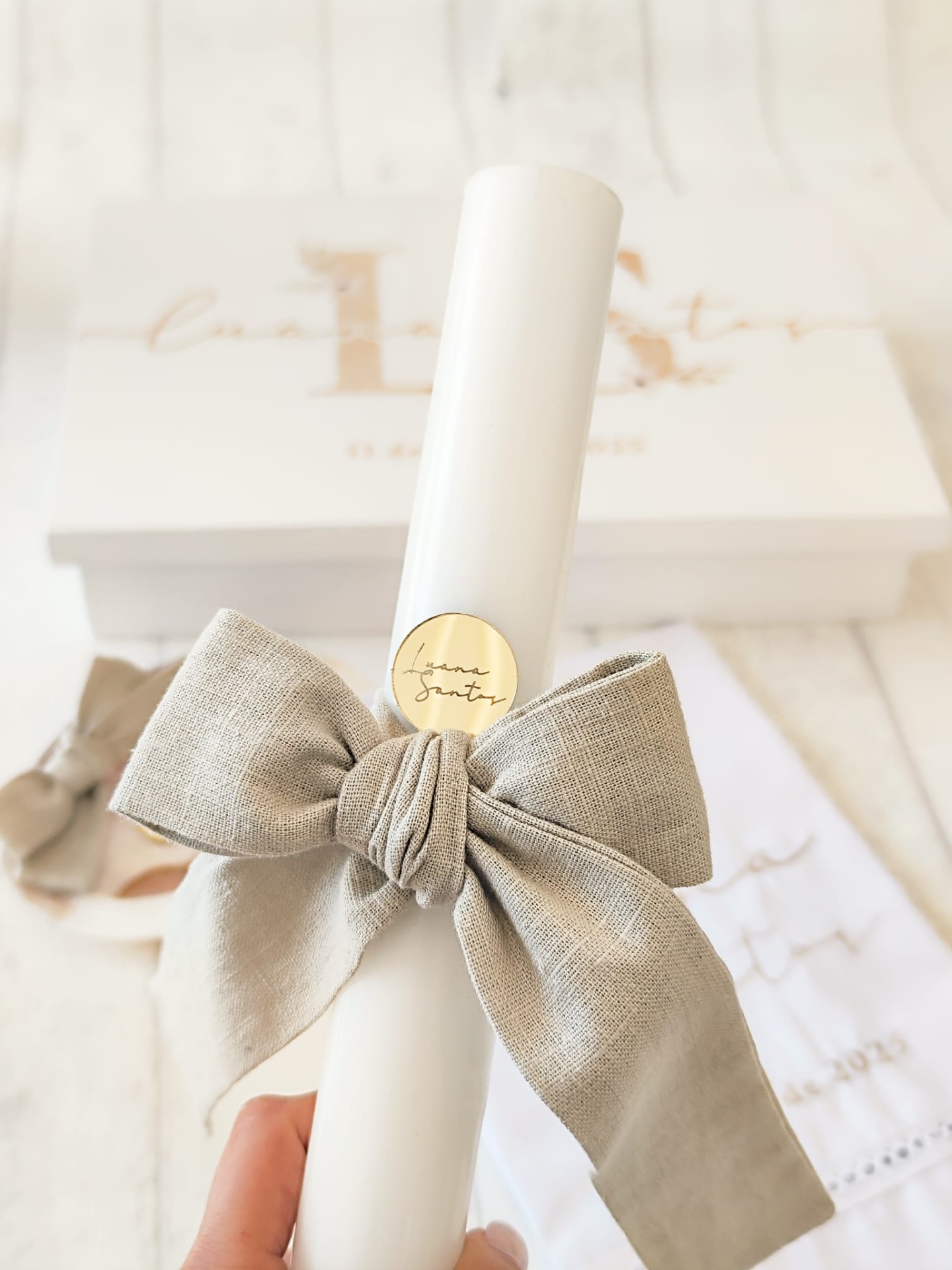 vela branca com laço cinzento e selo dourado, caixa branca ao fundo